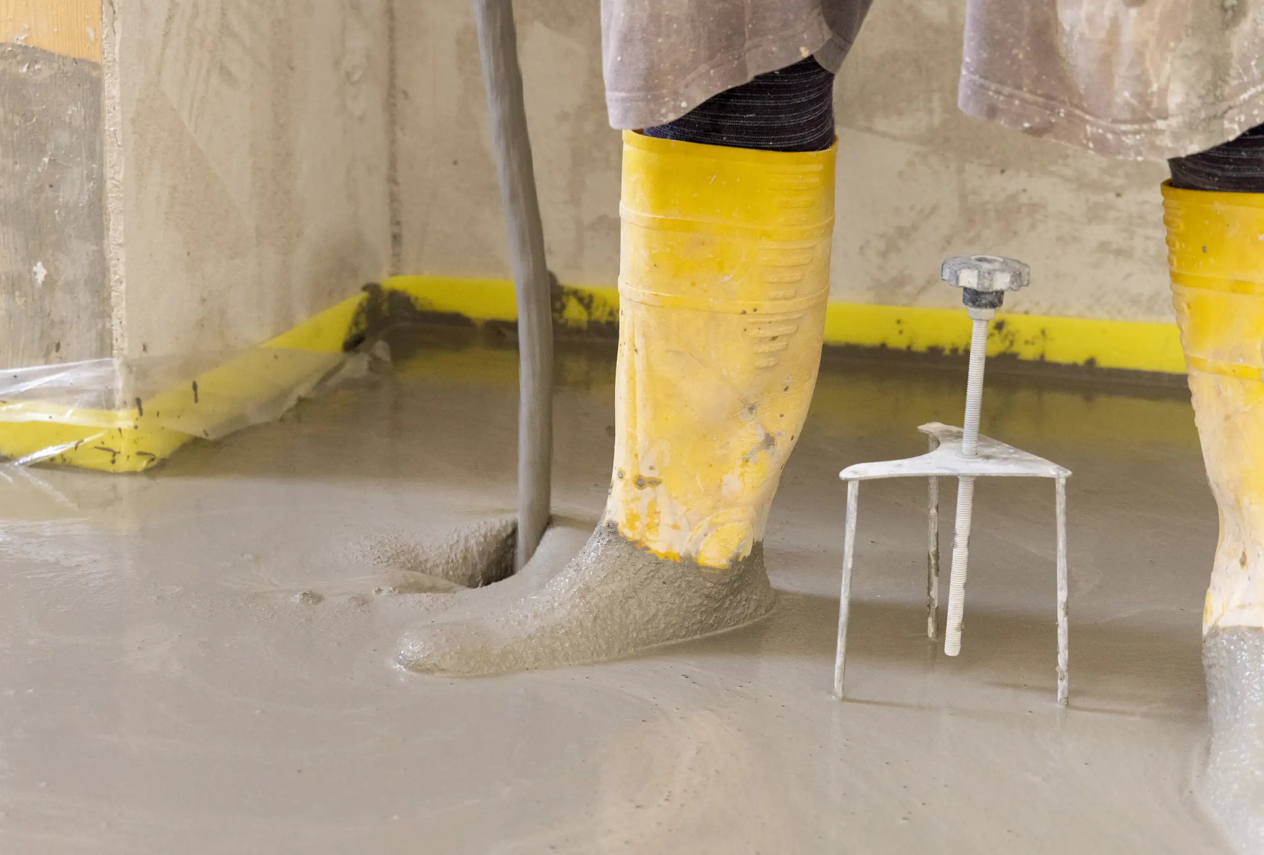 Fuß mit Gummistiefeln, der frischen Betonmischung bei der Untergrundvorbereitung für Epoxidharz Boden beschichtet